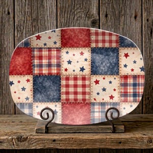 May include: Oval serving platter with a patchwork design in red, white, and blue. The platter features squares of plaid, stars, and textured patterns, reminiscent of a patriotic theme. It is displayed on a decorative metal stand.