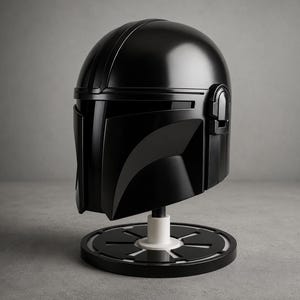 Puede incluir: Una r&eacute;plica de casco negro mandaloriano, exhibida sobre un soporte circular en blanco y negro. El casco tiene un acabado brillante con elementos de dise&ntilde;o detallados. El soporte tiene un soporte cil&iacute;ndrico blanco.
