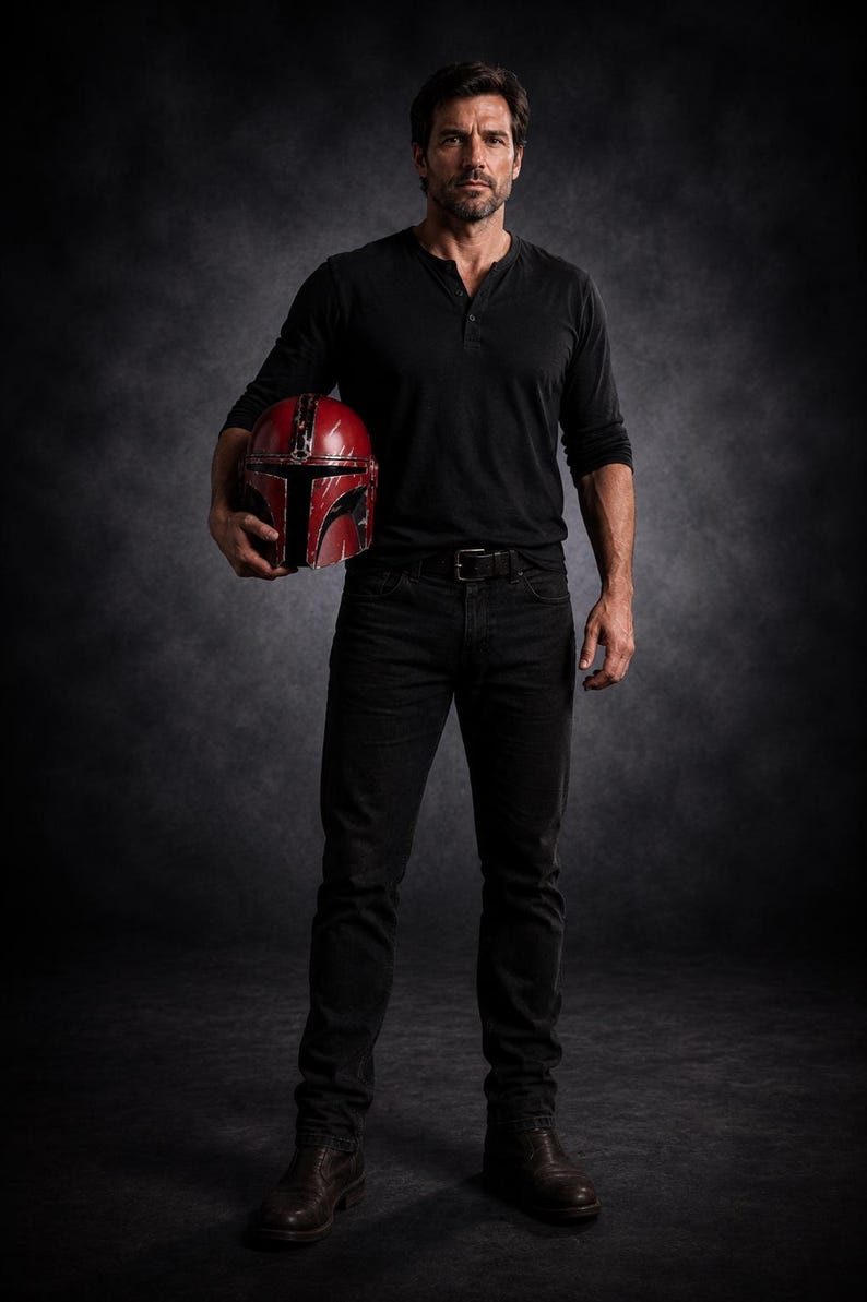 May include: A person wearing a black long-sleeve shirt and black jeans holds a red and black helmet. The helmet has a T-shaped visor and is likely a prop or costume piece. The person is wearing brown boots.