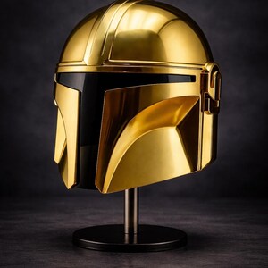 May include: A gold-colored Mandalorian helmet, displayed on a black stand. The helmet has a sleek, metallic finish with a black visor. The design features angular shapes and a prominent T-shaped visor.