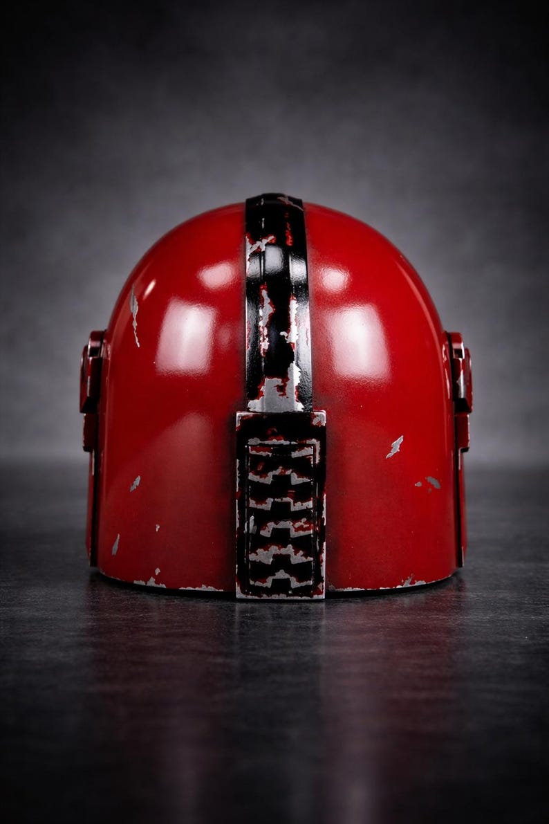 May include: A red helmet with a distressed finish, featuring a black stripe down the center and rectangular details on the back. The helmet has a glossy appearance with visible wear and tear.