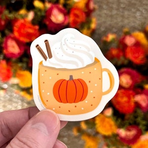 May include: A sticker of a pumpkin spice latte with whipped cream and cinnamon sticks. The mug is orange with white polka dots and a pumpkin on the front.