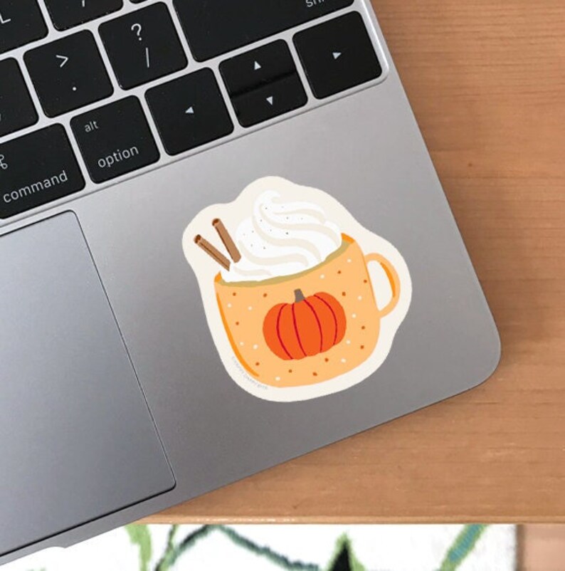 May include: A sticker of a pumpkin spice latte with whipped cream and cinnamon sticks. The latte is in a yellow mug with a pumpkin on the front.