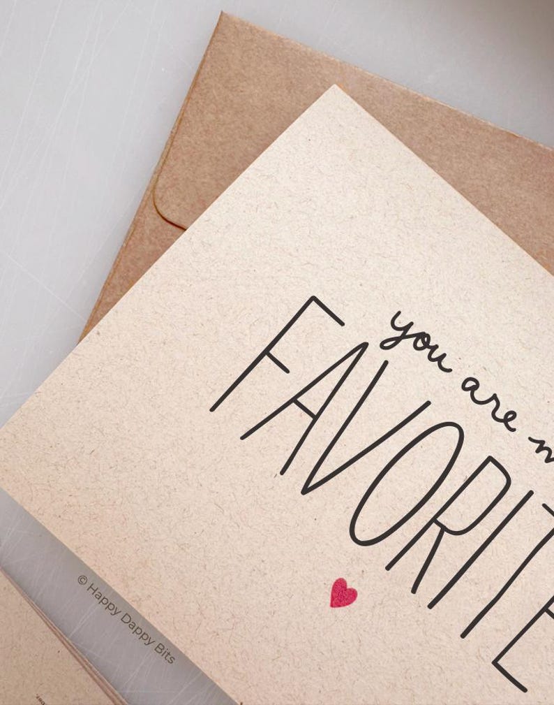 May include: A card with the text "you are my favorite" in black script font with a small red heart below the text. The card is on a brown paper background.