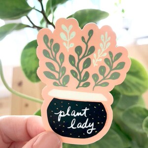 May include: A pink and black sticker with a potted plant and the text "plant lady".