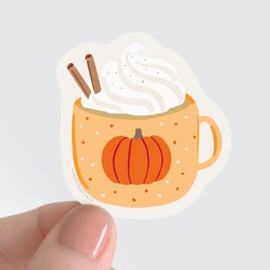 May include: A sticker of a pumpkin spice latte in a mug with whipped cream and cinnamon sticks. The mug has a white background with orange polka dots and a small pumpkin on the front. The text "Happy Daffy Bits" is on the bottom of the mug.