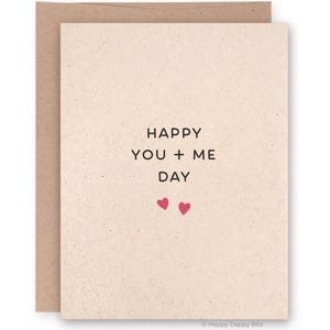 May include: A beige greeting card with the text "HAPPY YOU + ME DAY" in black, along with two small pink hearts. The card is inside a brown envelope. The bottom right corner has the text "Happy Dappy Bits".