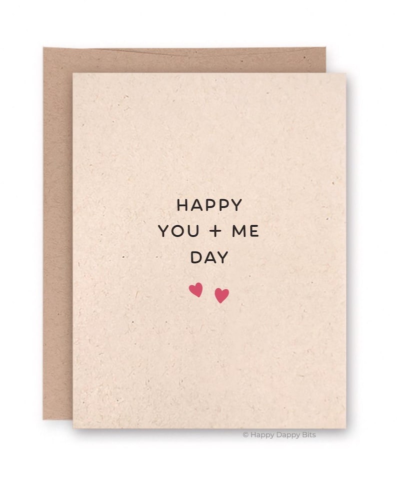 May include: A beige greeting card with the text "HAPPY YOU + ME DAY" in black, along with two small pink hearts. The card is inside a brown envelope. The bottom right corner has the text "Happy Dappy Bits".