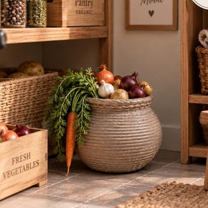 May include: A 1:12 scale miniature pantry scene featuring a round, rope-textured basket filled with a carrot, garlic, and onions. Nearby are wooden crates labelled 'Pantry Organic' and 'Fresh Vegetables', glass jars, and a sign reading 'Good Food Good Mood'.
