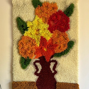 Peut inclure: Tapisserie murale texturée représentant un arrangement floral dans un vase. Les fleurs sont dans des tons de jaune, d'orange et de rouge, avec des feuilles vertes. Le vase est rouge foncé et le fond est beige.