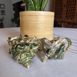 Peut inclure: Un ensemble sucrier et pot à lait en céramique en forme de coquillages épineux. Les deux pièces présentent un vernis brillant marbré vert et crème avec des crêtes et des pointes texturées imitant l'aspect naturel d'un coquillage marin.