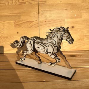 Puede incluir: Escultura de caballo de madera en pose de carrera, con un diseño en capas con rayas blancas y negras. La escultura está montada sobre una base rectangular y tiene los números "2-1", "2-3" y "8-10" impresos.
