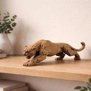 Puede incluir: Escultura de madera de un tigre en posición agachada, con tallado detallado. El tigre es marrón y está sobre una estantería de madera. Es un objeto decorativo.