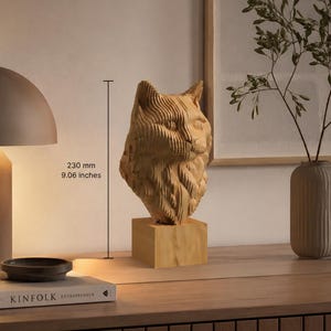 May include: A light-colored wooden cat head sculpture composed of layered, horizontal slices, mounted on a square base. The sculpture measures 9.06 inches in total height, featuring detailed carved fur textures and pointed ears.