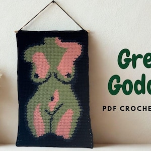 以下が含まれることがあります： 黒い背景に、緑とピンクで描かれた女性の姿の、かぎ針編みの壁掛け。テキスト「Green Goddess PDF Crochet Pattern」は緑色で表示されています。木製の棒から吊り下げられたアートワーク。