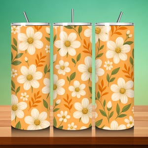 May include: Three stainless steel tumblers with lids and straws. Each tumbler has a repeating pattern of white daisies with yellow centres, green leaves, and orange accents on an orange background. The tumblers are designed for cold drinks.