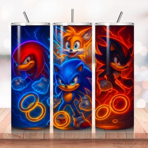May include: Three stainless steel tumblers with illustrations of Sonic the Hedgehog characters. Each tumbler features a different character: Knuckles, Sonic, Tails, and Shadow, with vibrant neon-like effects and a straw.