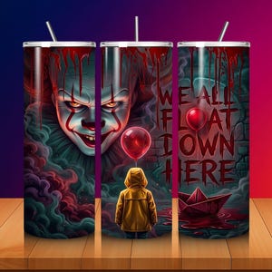 May include: A cylindrical tumbler with a straw featuring a graphic print of a clown face, a person in a yellow raincoat, a red balloon, and a paper boat. The text WE ALL FLOAT DOWN HERE is printed in red against a dark, moody, and smoky background.