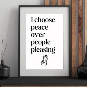 May include: Framed art print with the message "I choose peace over people-pleasing" in black text on a white background. The print includes a peace sign with a heart. The frame is black.