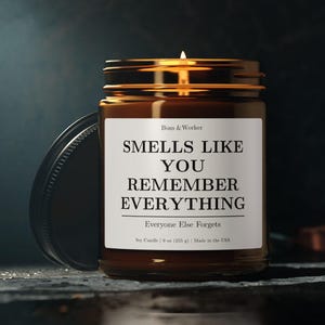 以下が含まれることがあります： 黒い持ち手と「But First, Coffee」の太字の黒い文字が入った白いセラミックマグ。マグカップはぼやけた背景に置かれており、居心地の良い環境を示唆しています。