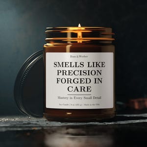以下が含まれることがあります： 黒い蓋が付いた茶色のガラス瓶に入った、火のついた大豆キャンドル。「Smells Like Precision Forged in Care」と書かれたラベル。キャンドルは255gで、米国製です。「Boss & Worker」のブランド名がラベルの上部にあります。