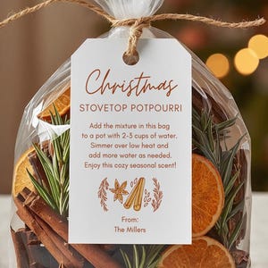 May include: A clear cellophane bag tied with twine, filled with dried orange slices, cinnamon sticks, star anise, and rosemary. A white tag reads "Christmas STOVETOP POTPOURRI" with instructions. The bag is a festive, seasonal home fragrance.