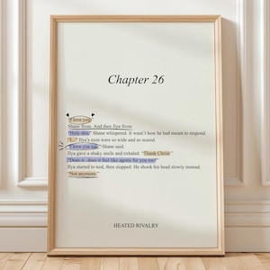 Puede incluir: Una impresión enmarcada con el texto "Chapter 26" en la parte superior. El texto incluye frases como "I love you" y "Holy shit". La parte inferior de la impresión dice "HEATED RIVALRY". El marco es de color marrón claro.