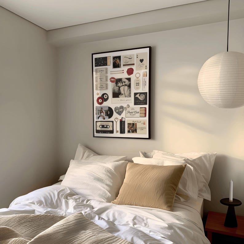 May include: A framed collage of vintage-style images and ephemera hangs above a bed with white linens and a tan pillow. The collage includes photos, cards, and other decorative elements. A paper lantern and a candle complete the room's decor.