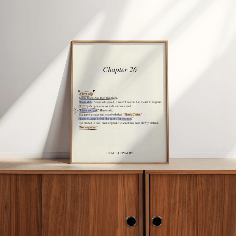 May include: A framed print with text from "Chapter 26" of a book. The text includes phrases like "I love you too" and "Does it feel like agony for you too?" The print is in a wooden frame and rests on a wooden cabinet.