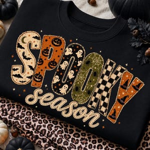 May include: A black crewneck sweatshirt featuring the text SPOOKY season in large, decorative letters. Each letter has a unique pattern including bats, pumpkins, ghosts, spiderwebs, checkered squares, and witch hats in orange, black, and cream.