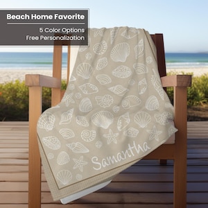May include: A beige beach towel with a white seashell and starfish pattern, draped over a wooden chair. The name "Samantha" is printed in white on the towel. The text "Beach Home Favorite" and "5 Color Options Free Personalization" is in the top left corner.