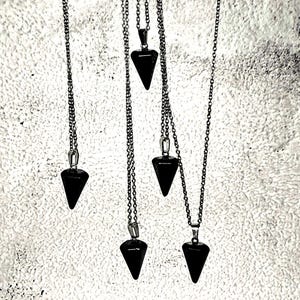 May include: Six black crystal pendulums hanging from silver chains. Each pendulum has a triangular shape and is suspended against a textured, off-white background. The chains are delicate and the crystals are polished.