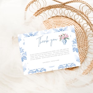 Może przedstawiać: Biała karta z niebieską kwiatową obwódką i napisem „Thank you”. Niebiesko-biała waza z różowymi kwiatami znajduje się w prawym górnym rogu. Karta zawiera miejsce na niestandardową wiadomość.