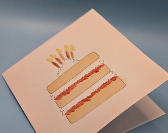 May include: A folded greeting card featuring a watercolor illustration of a layered cake with frosting and candles. The cake has three layers with red filling and white frosting. The card is open, revealing a blank interior, against a blue background.