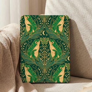 May include: A green and gold patterned case featuring a repeating design of frogs, leaves, and flowers. The case has a dark green background with gold accents and a symmetrical layout. The design includes a crescent moon and a butterfly.