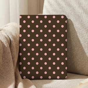 May include: A rectangular tablet or e-reader case featuring a dark brown background with a repeating pattern of small, evenly spaced light pink polka dots. The case has a smooth, flat surface and rounded corners, presenting a clean and simple design.