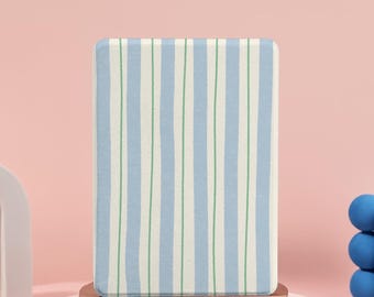 Puede incluir: Un objeto rectangular con rayas azules y blancas, acentuado con líneas verdes, presentado sobre un pequeño pedestal redondo marrón. El fondo es rosa, con un arco blanco y esferas azules.