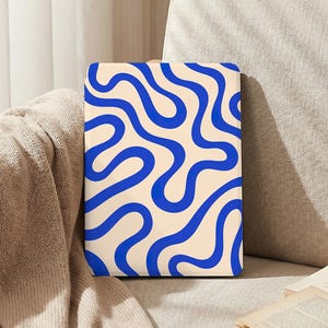 Puede incluir: Una funda rectangular crema para cuaderno o tableta con un patrón repetido de líneas onduladas azules. Descansa sobre una superficie beige, creando un ambiente relajado y acogedor.
