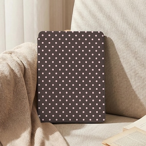 May include: A rectangular, dark brown case featuring a repeating pattern of small, evenly spaced pink polka dots. The case is resting on a beige surface, possibly fabric. The design is simple and classic, with a vintage feel.