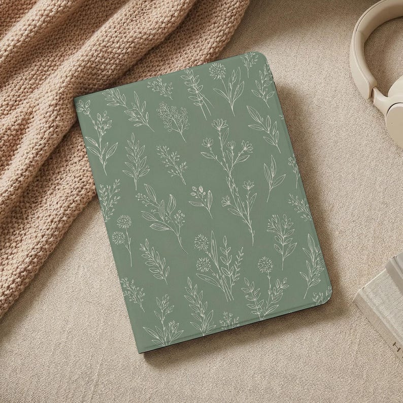 May include: A rectangular tablet case featuring a sage green background with a repeating white line art pattern of various wildflowers, stems, and leaves. The case has a smooth, flat surface and covers the entire front of the electronic device.