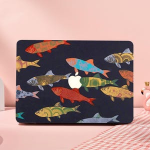May include: A laptop case with a dark blue background, decorated with colourful fish illustrations. The fish are in various colours and designs, including orange, yellow, and blue. A white apple logo is in the centre.