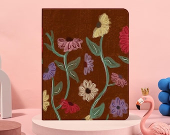 May include: A brown notebook with a floral design featuring colorful flowers in shades of pink, yellow, and purple. The flowers have green stems and leaves. The notebook is displayed on a pink pedestal.