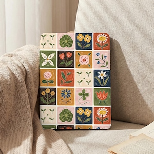 May include: A tablet case featuring a colorful floral pattern. The design is composed of a grid of squares, each containing a different flower illustration in shades of yellow, pink, blue, and green. The case is shown resting on a beige surface.