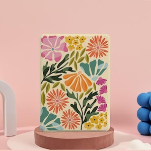 May include: A rectangular case with a floral design. The case features a cream background with colorful flowers in shades of pink, orange, teal, and yellow, along with green leaves. The case is displayed on a small, round, brown pedestal.