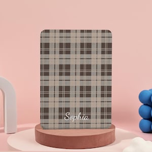 May include: A rectangular item with a brown, grey, and beige plaid pattern and rounded corners. The name "Sophia" is written in white at the bottom. It is displayed on a small, round, brown pedestal.