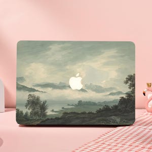 Könnte beinhalten: Laptop-Hülle mit Landschaftsmalerei in Grün, Grau und Weiß. Das Design zeigt eine neblige Berglandschaft mit Bäumen und Wasser. Das Apple-Logo ist sichtbar.