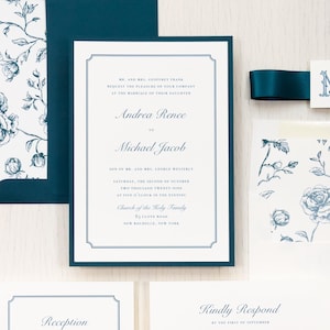 May include: A white wedding invitation card with dark blue text and a thin dark blue border. The invitation features the names Andrea Rence and Michael Jacob, with matching dark blue envelopes featuring a white and blue floral pattern.