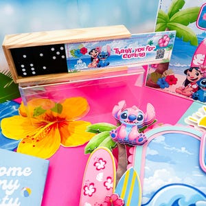 May include: A wooden domino set with black dominoes and white dots, featuring a decorative label with cartoon characters and the text "Thank you for coming." The scene includes tropical-themed party decorations with surfboards and flowers.