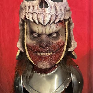 Puede incluir: Un busto detallado y pintado a mano de una criatura demoníaca de la película Army of Darkness. La criatura lleva un casco con forma de cráneo y armadura, con una cara sangrienta y horrible. El busto está montado sobre una base de madera con las palabras "Army of Darkness" impresas en rojo.