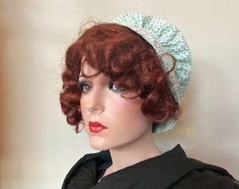 Puede incluir: Un gorro de tela blanco y verde con estampado y un volante fruncido alrededor del borde. El gorro se lleva en un maniquí con el pelo rojo rizado.